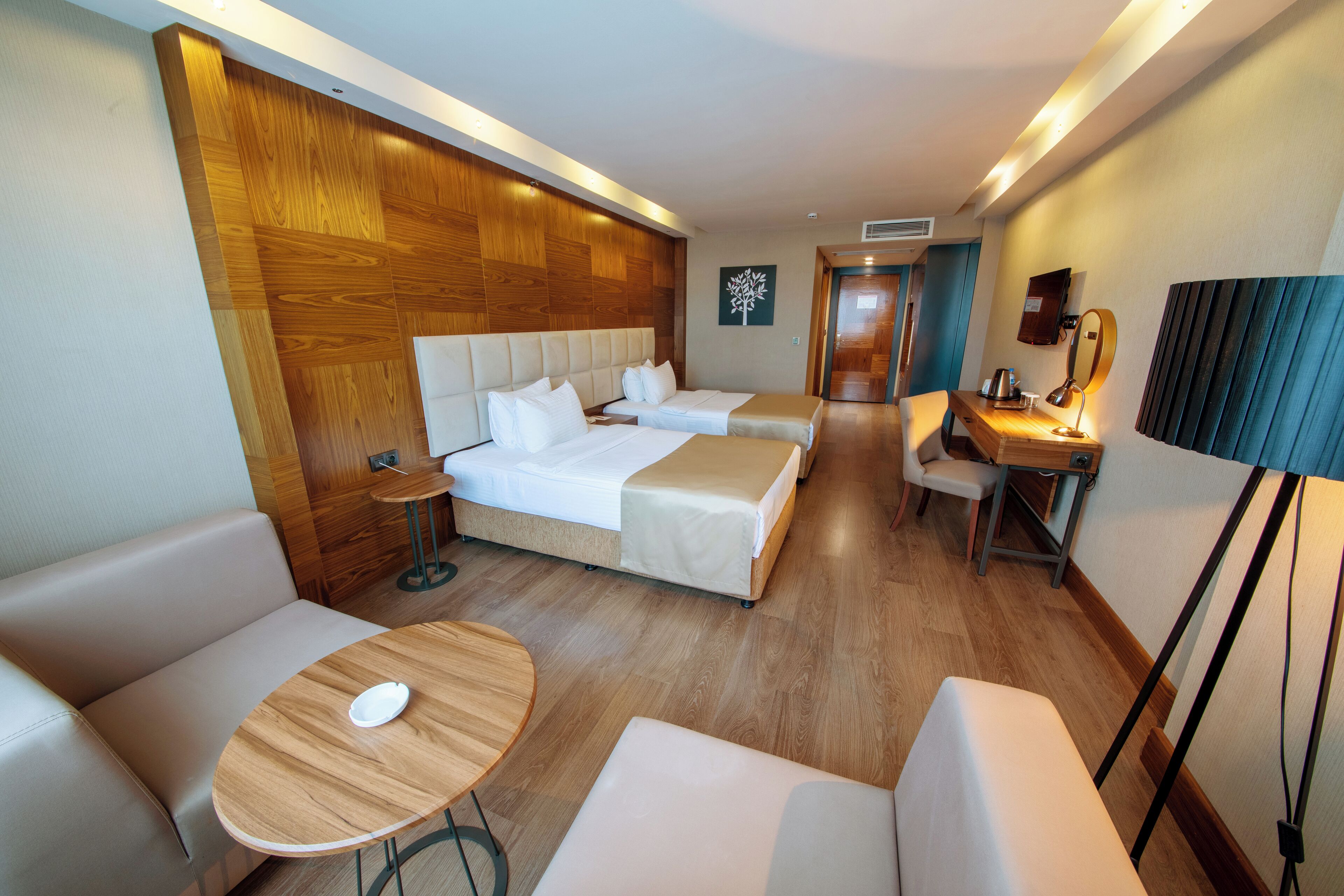 A hotel room with a wooden headboard, two beds, a desk with a chair, a round table, and a lamp.