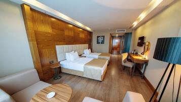 Habitación de hotel con cabecera de madera, dos camas, un escritorio con silla, una mesa redonda y una lámpara.