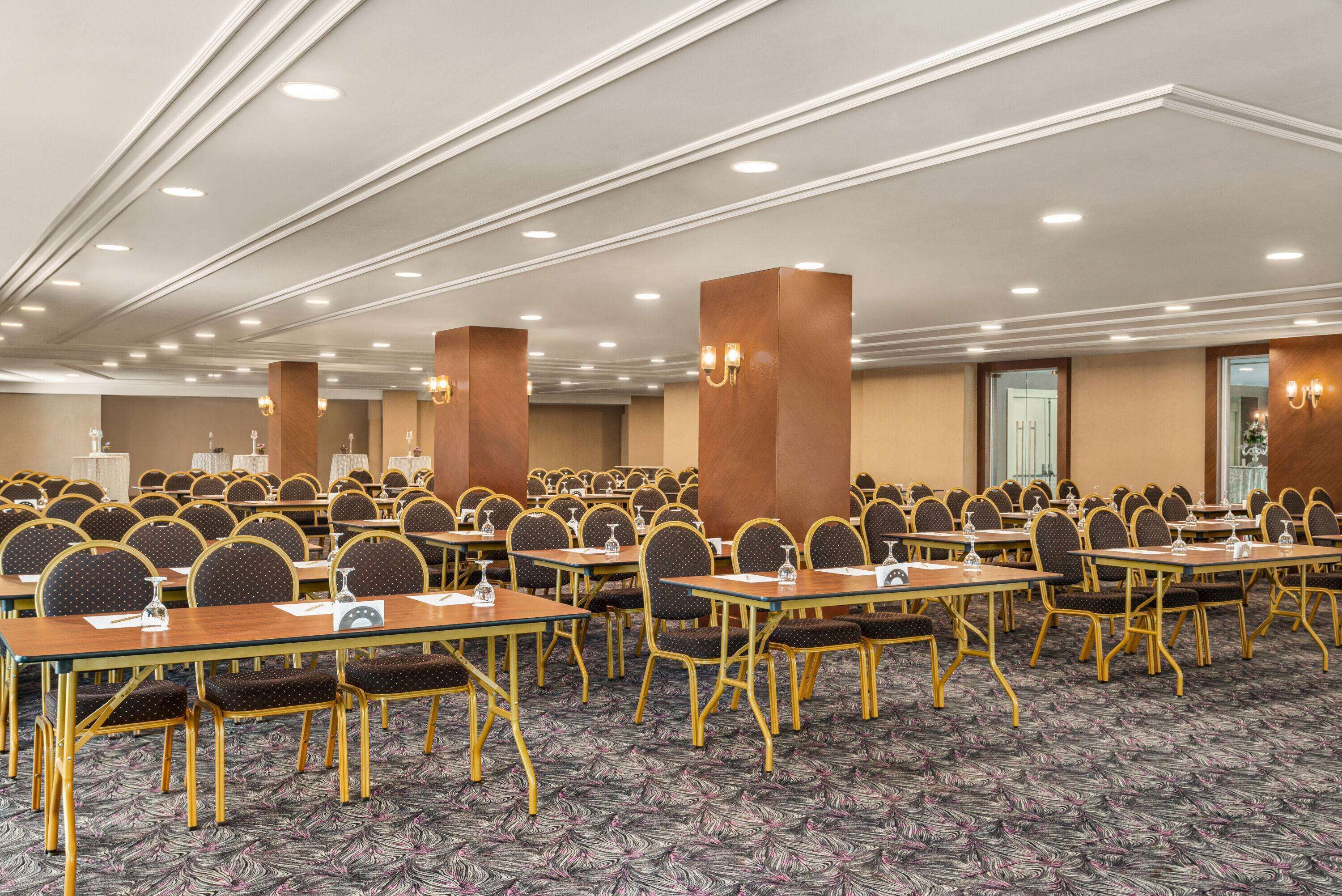 Une salle de conférence avec des rangées de tables et de chaises, un éclairage encastré et une moquette à motifs.