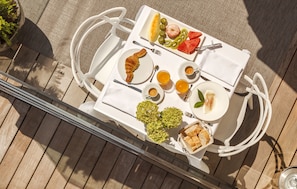 Una mesa de comedor con un croissant, fruta y bebidas en una terraza soleada.