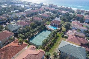 An aerial view of a coastal residential area with houses, a swimming pool, and a beach in the background.