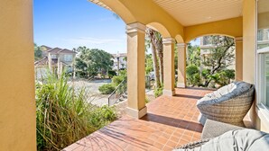 Un porche cubierto con una silla de mimbre y vistas a casas vecinas y follaje.