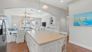 Una cocina amplia con una isla central, muebles blancos y un ventanal que proporciona luz natural.
