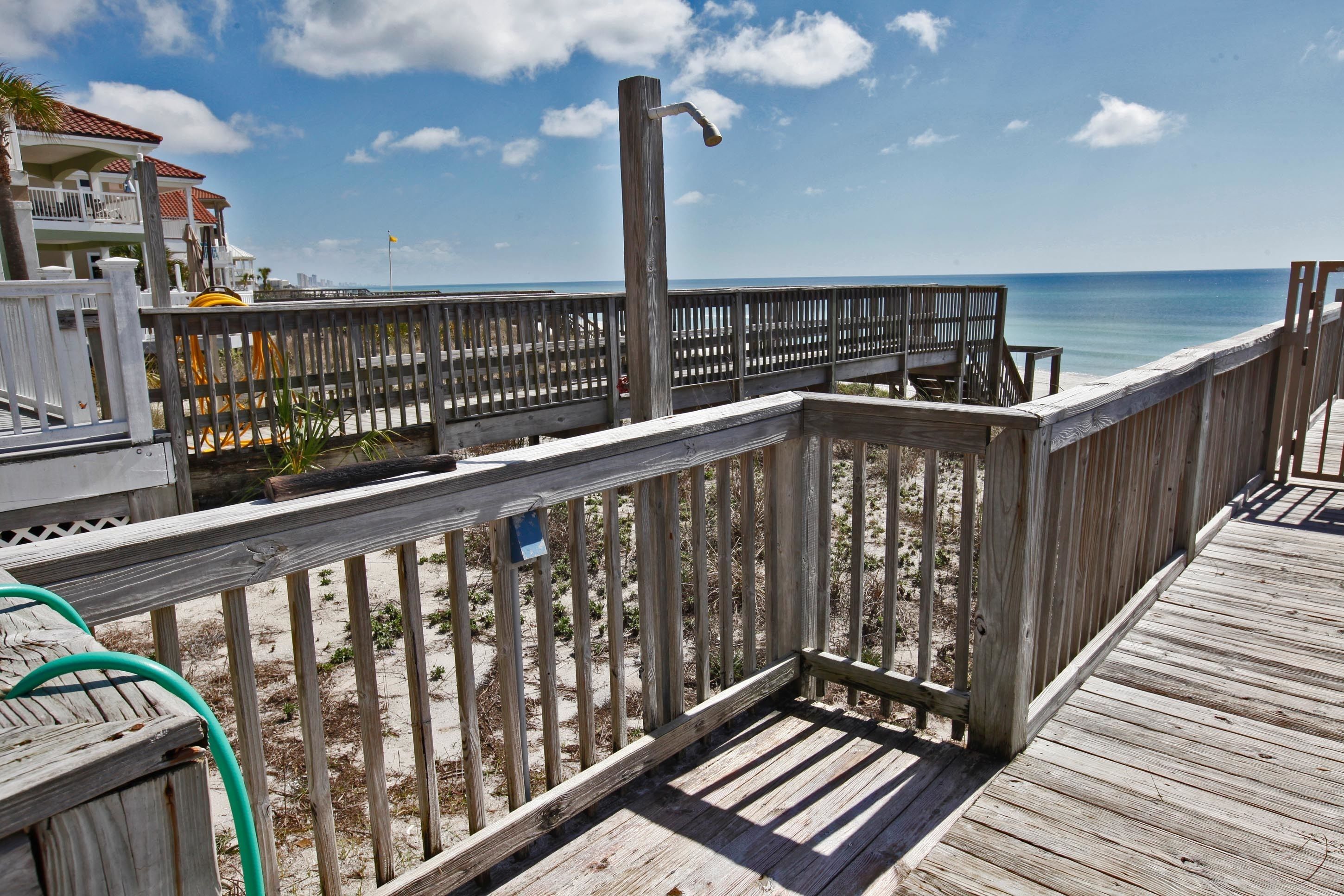 A wooden deck with a railing overlooking a beach, a clear sky, and a distant view of the ocean.