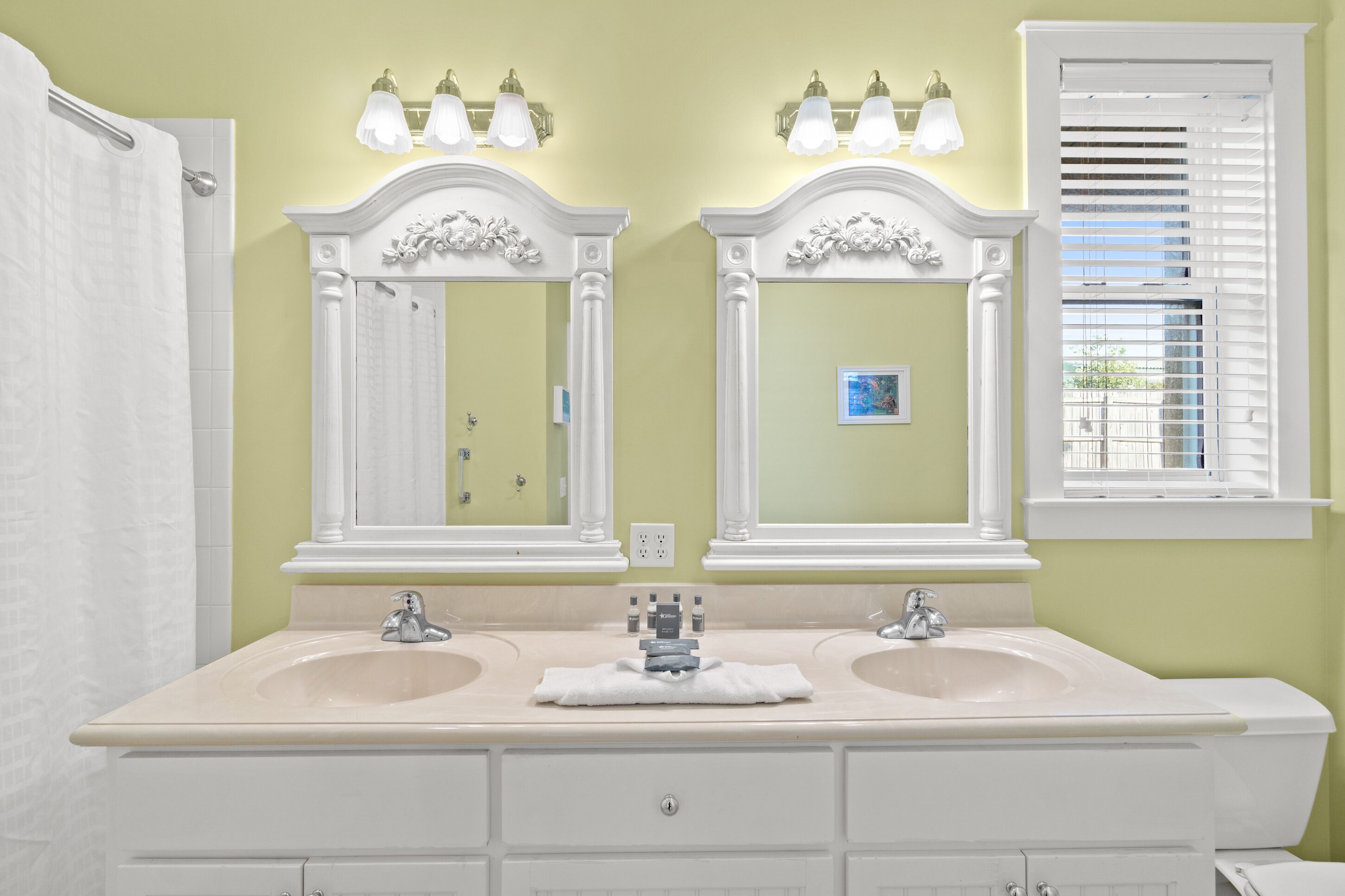 A bathroom with two sinks, a shower, and a window with blinds.