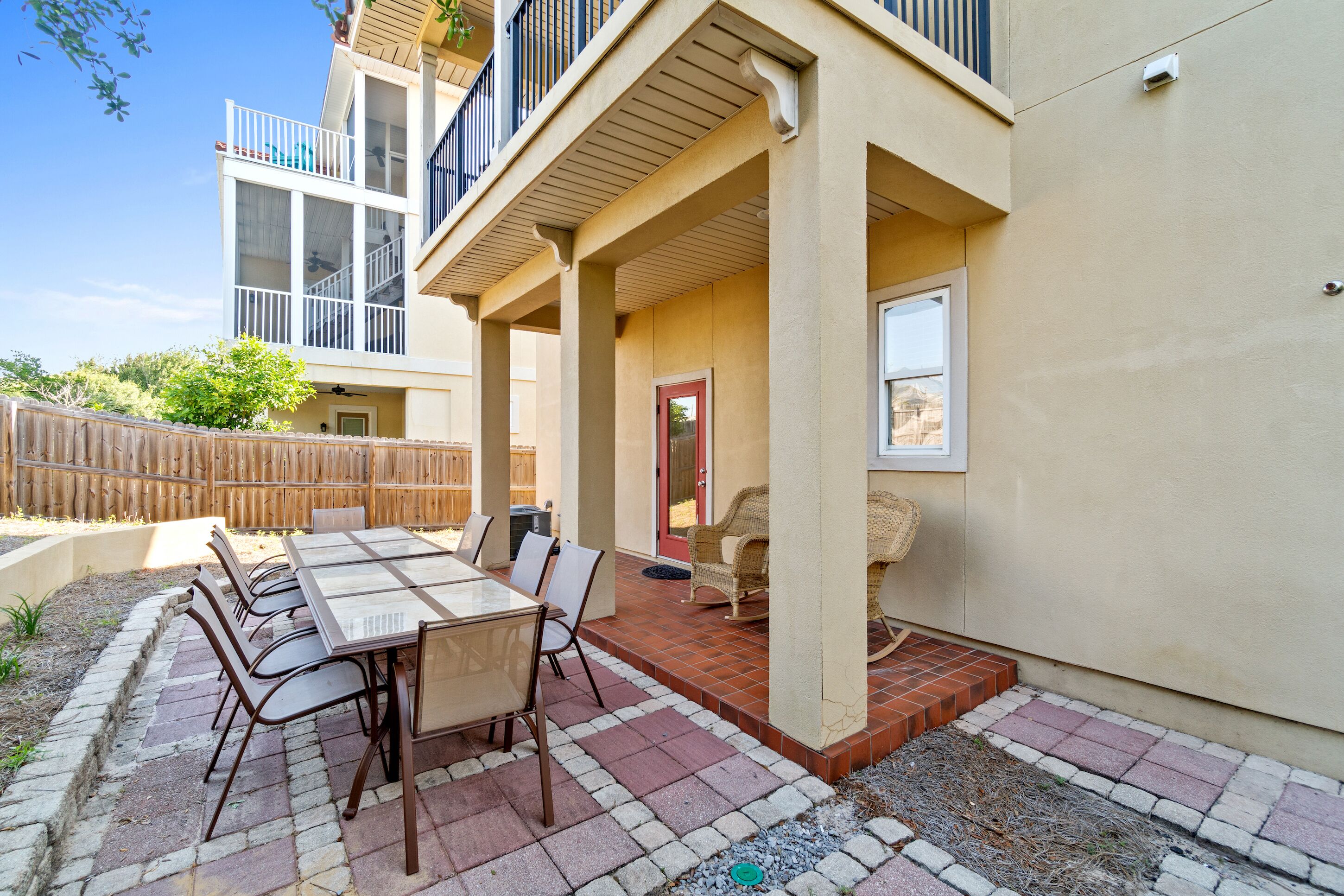 A patio with a glass-top table and chairs, a wooden fence, and a building with a balcony.