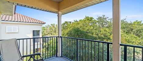 A covered balcony with a chair, a railing, and a view of a house and trees.
