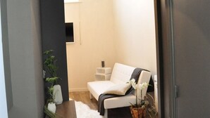 A modern living room with a white sofa, a small side table, and a potted plant. - Lille A Part - Gites Urbains (Lille)