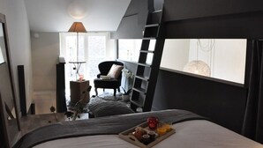 A modern bedroom with a loft bed, a bedside table with a lamp, a chair, and a tray with breakfast items. - Lille A Part - Gites Urbains (Lille)