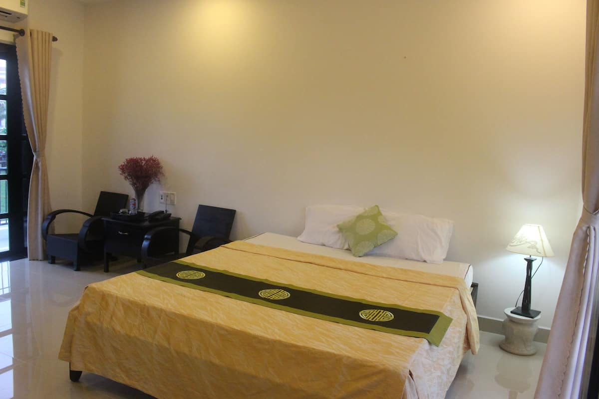 A hotel room with a bed, a desk, a chair, a lamp, and a vase with flowers.