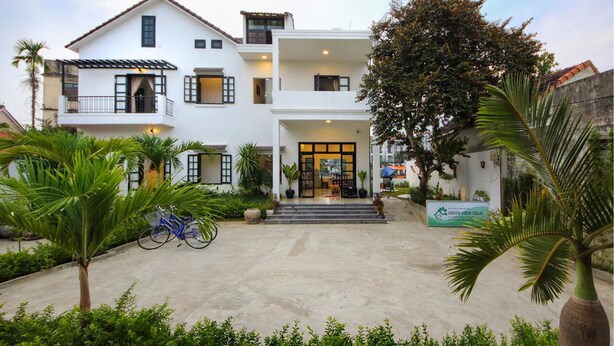 Edifici de dues plantes amb entrada central, envoltat de vegetació i un rètol que diu 'Green View Villa'.