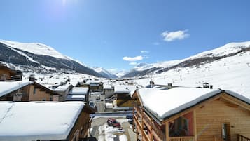 Un pueblo cubierto de nieve con edificios de madera, cielo despejado y montañas al fondo.