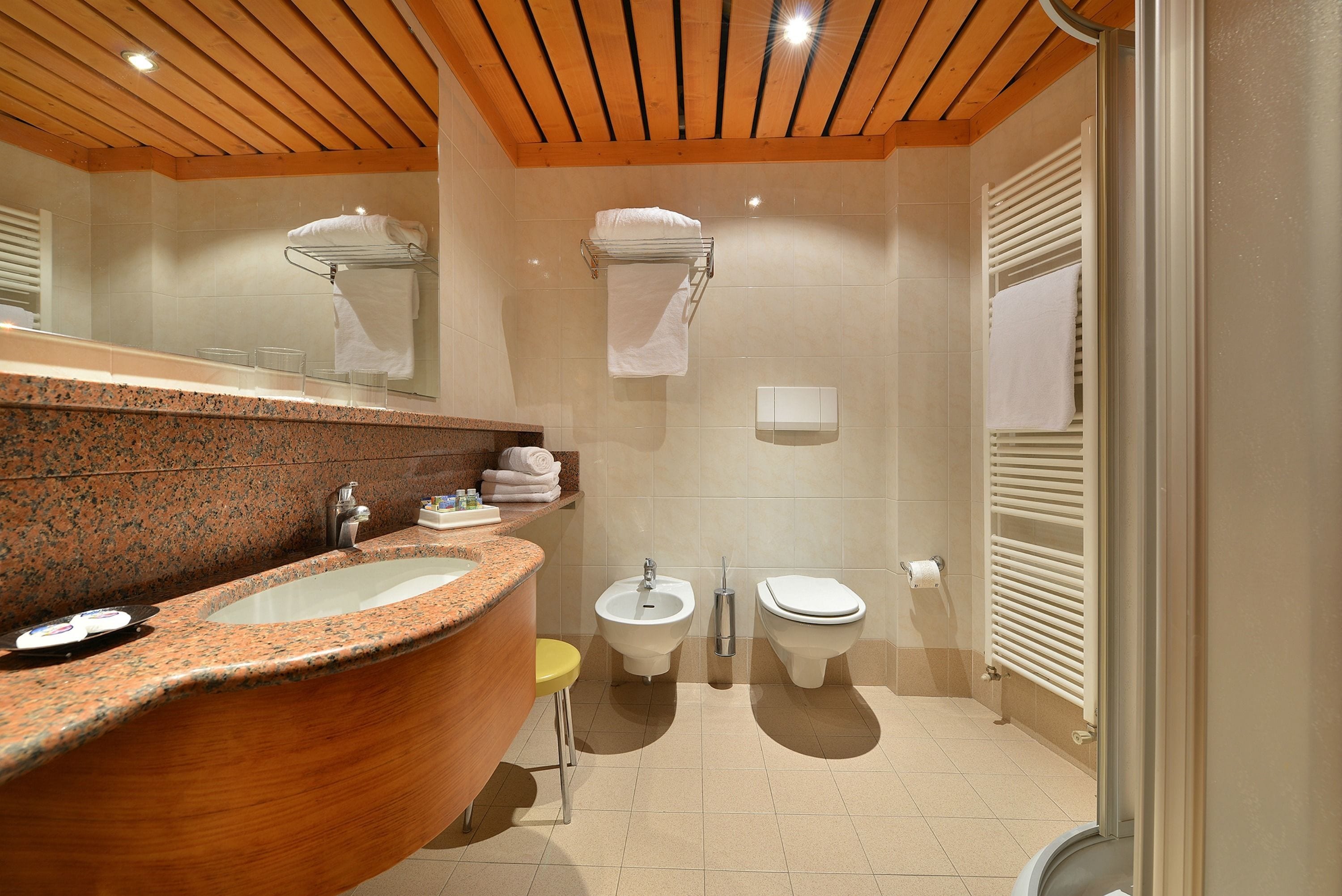 Un baño con tocador de madera, lavamanos, bidé, inodoro y toalleros.