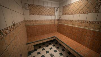 Une salle de bain avec des murs carrelés, un espace douche et un sol à carreaux.