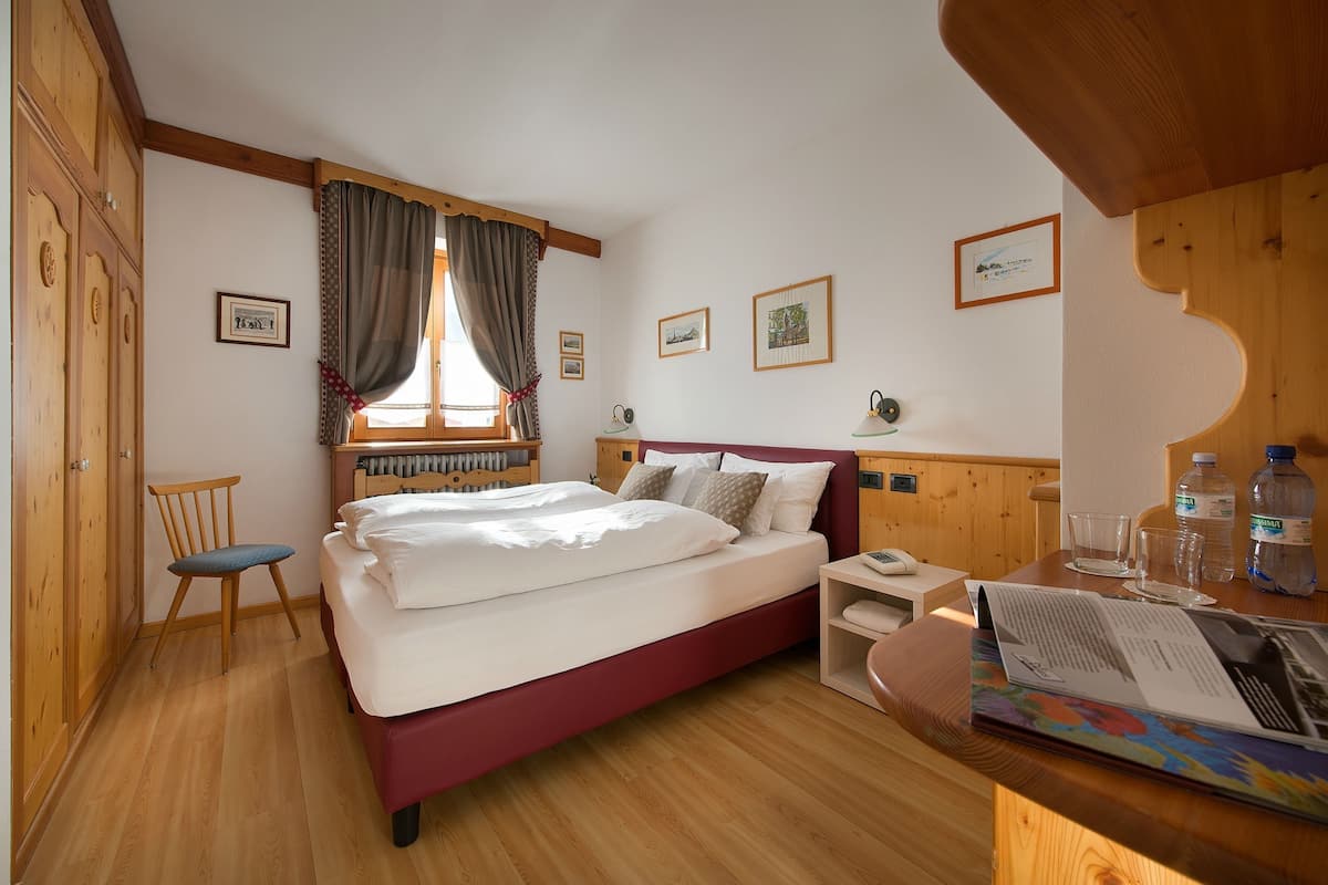 Une chambre à coucher avec un lit, une armoire en bois, une chaise, un bureau avec une lampe et des tableaux encadrés accrochés au mur.