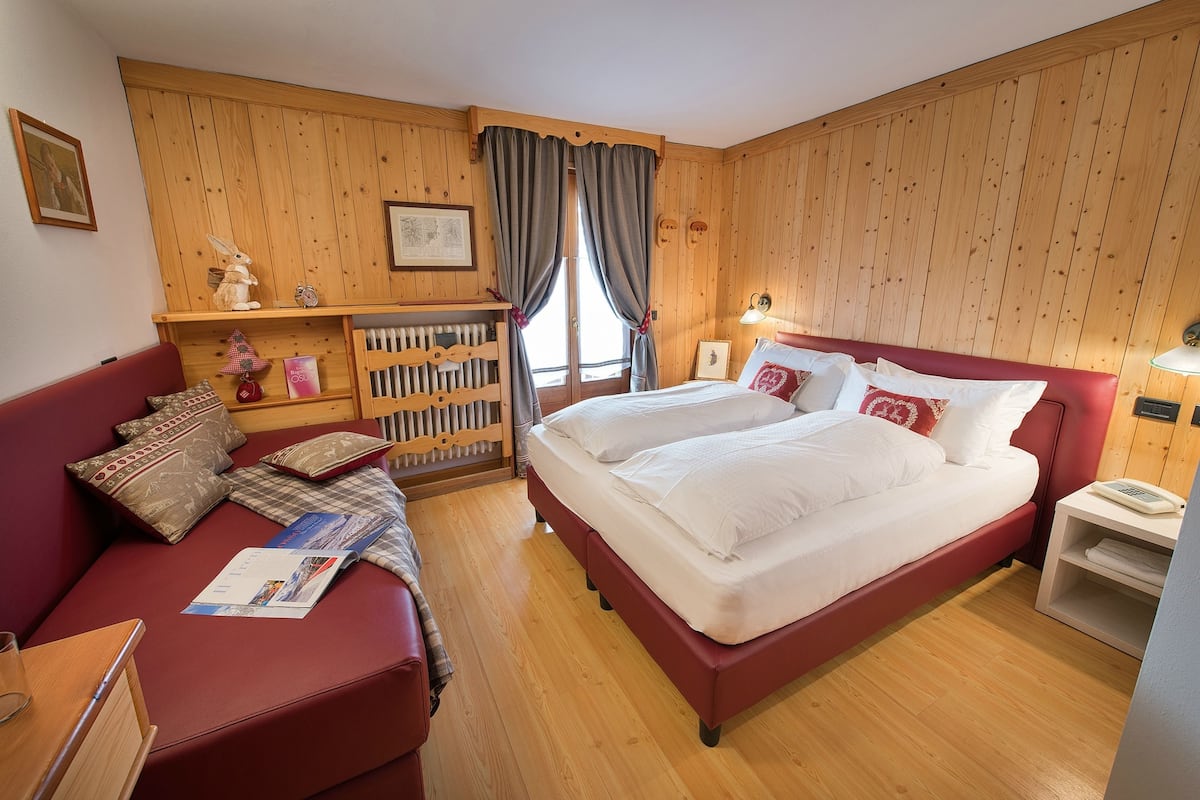 Une chambre avec un canapé rouge, deux lits simples, un lambris en bois, un radiateur et une table de chevet avec une lampe.