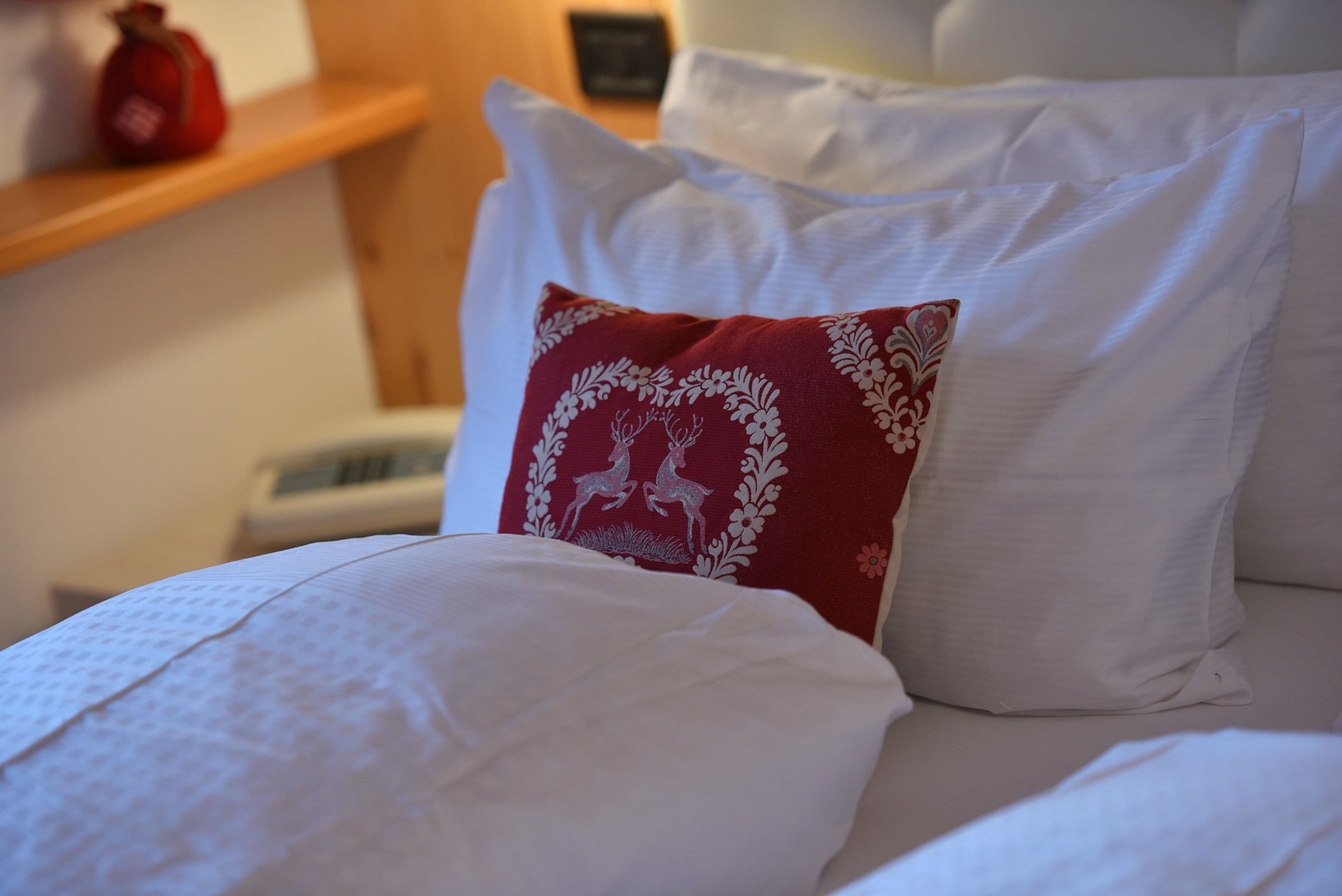 A bed with white bedding and a red pillow with a deer design.