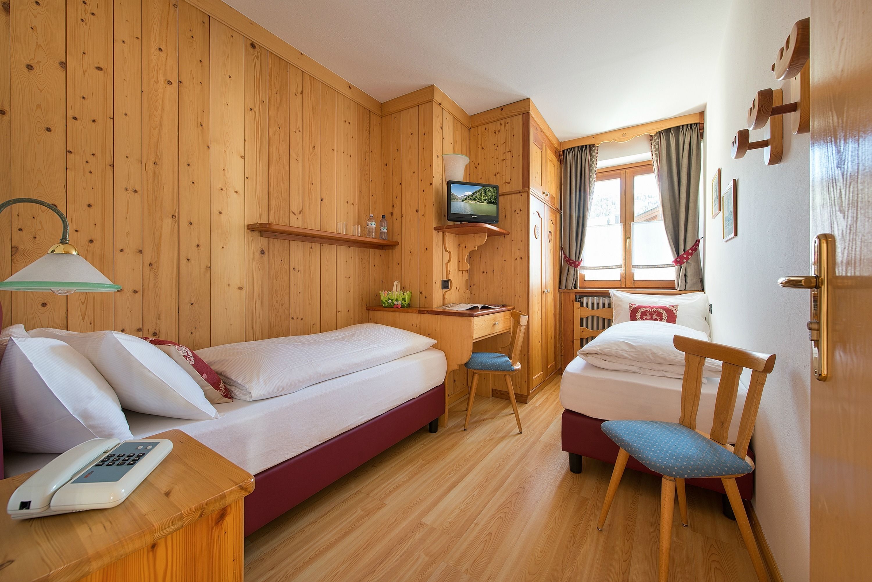 A wooden-paneled room with a bed, desk, chair, and a television on a shelf.