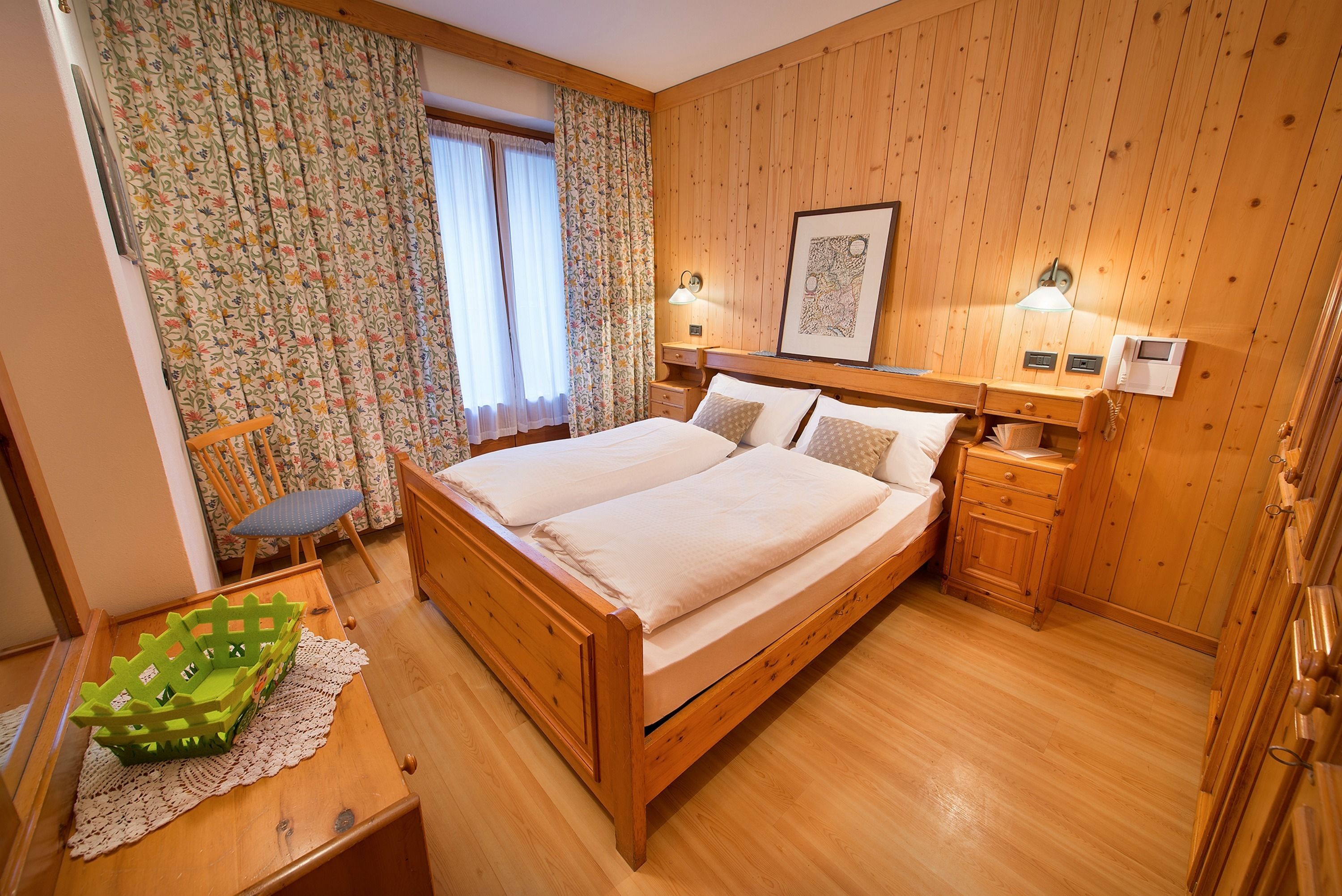Camera da letto con rivestimento in legno, un letto matrimoniale, comodini, una sedia e una scrivania con un cesto.