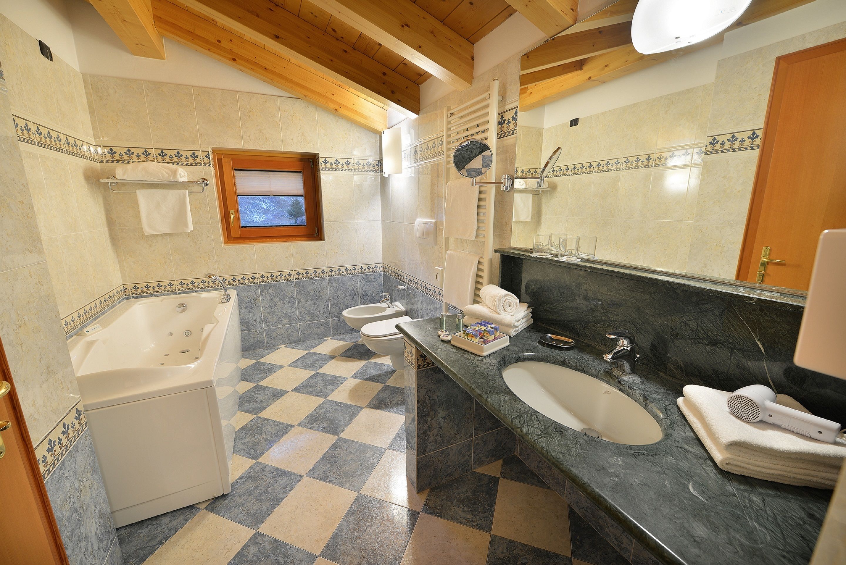 A bathroom with a checkered floor, a bathtub, a sink, and a large mirror.