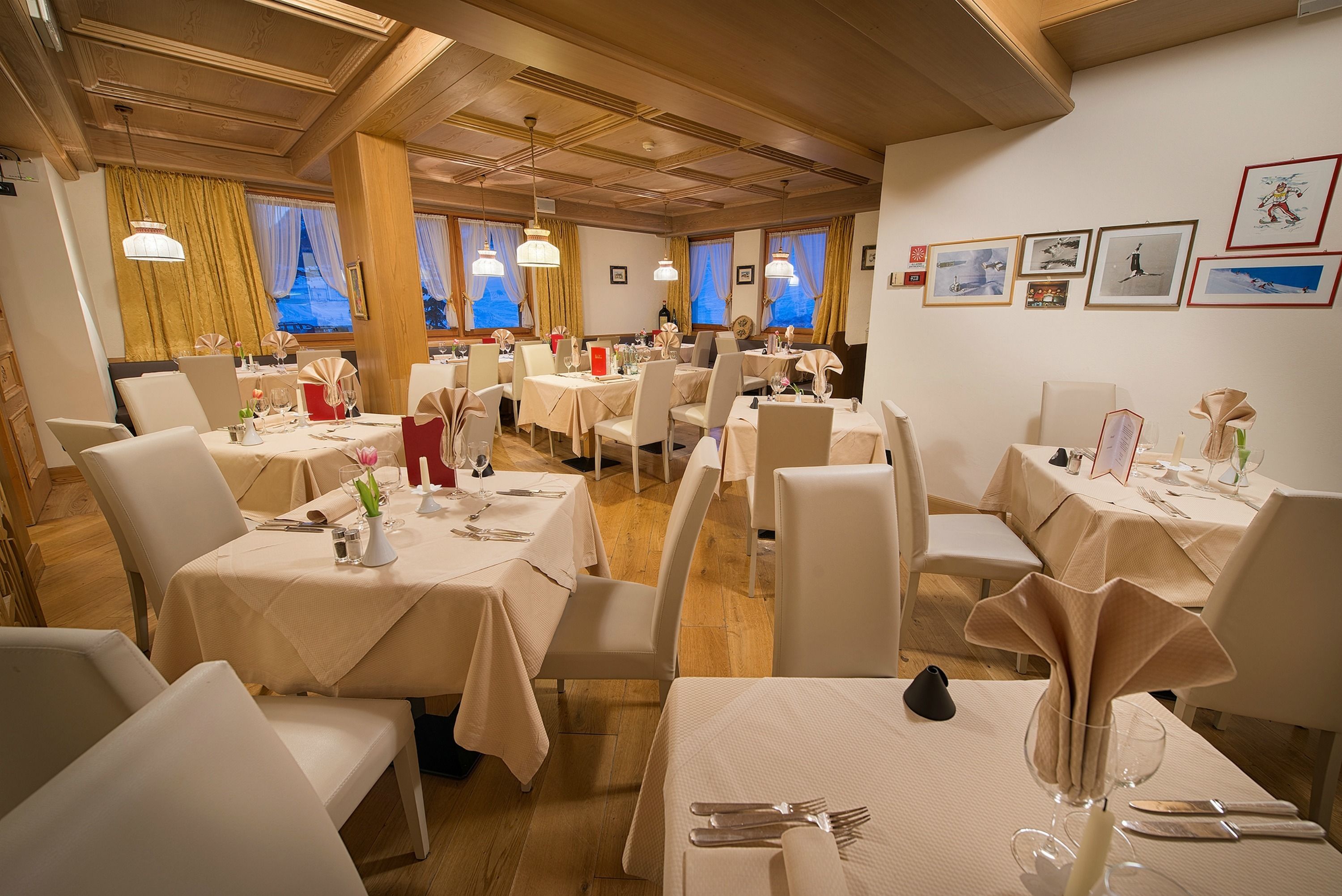 A restaurant with multiple tables set for dining, featuring a warm wooden interior and large windows with curtains.