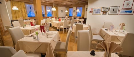 A restaurant with multiple tables set for dining, featuring a warm wooden interior and large windows with curtains.