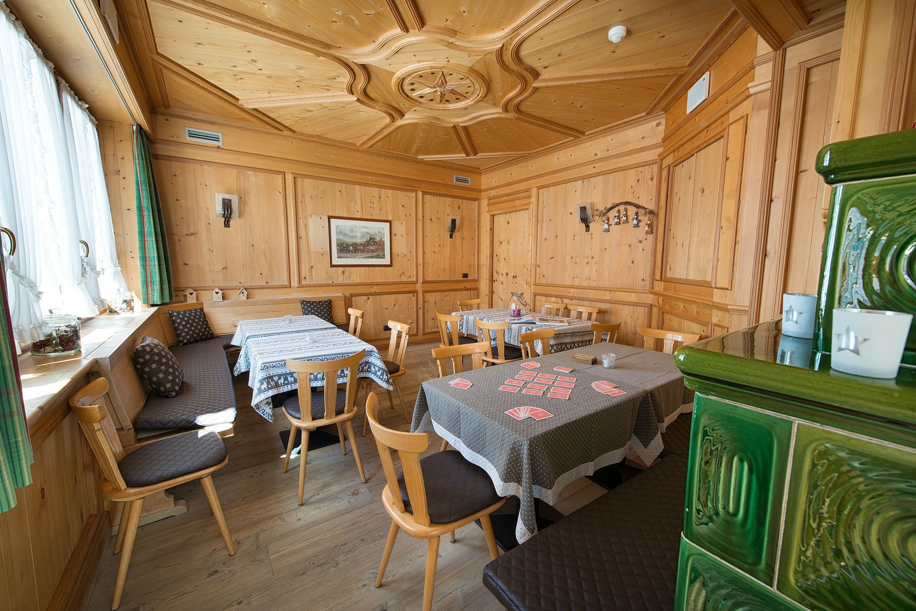 A wooden cabin interior with multiple dining tables, chairs, and a green cabinet.