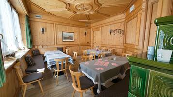 Interior de una cabaña de madera con varias mesas de comedor, sillas y un armario verde.