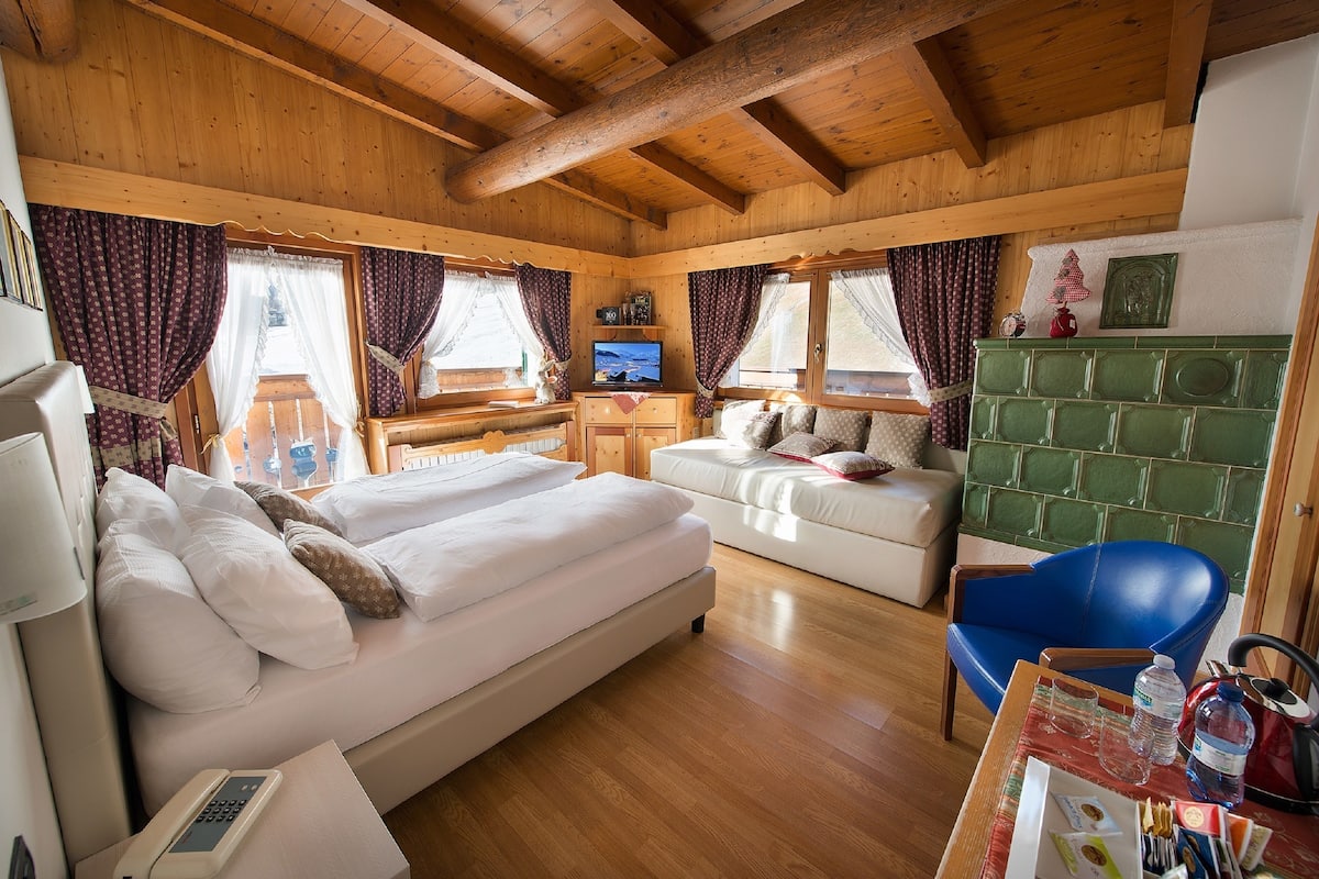 L’intérieur d’un chalet en bois comprend un lit, un canapé, un bureau avec une télévision et un meuble vert.