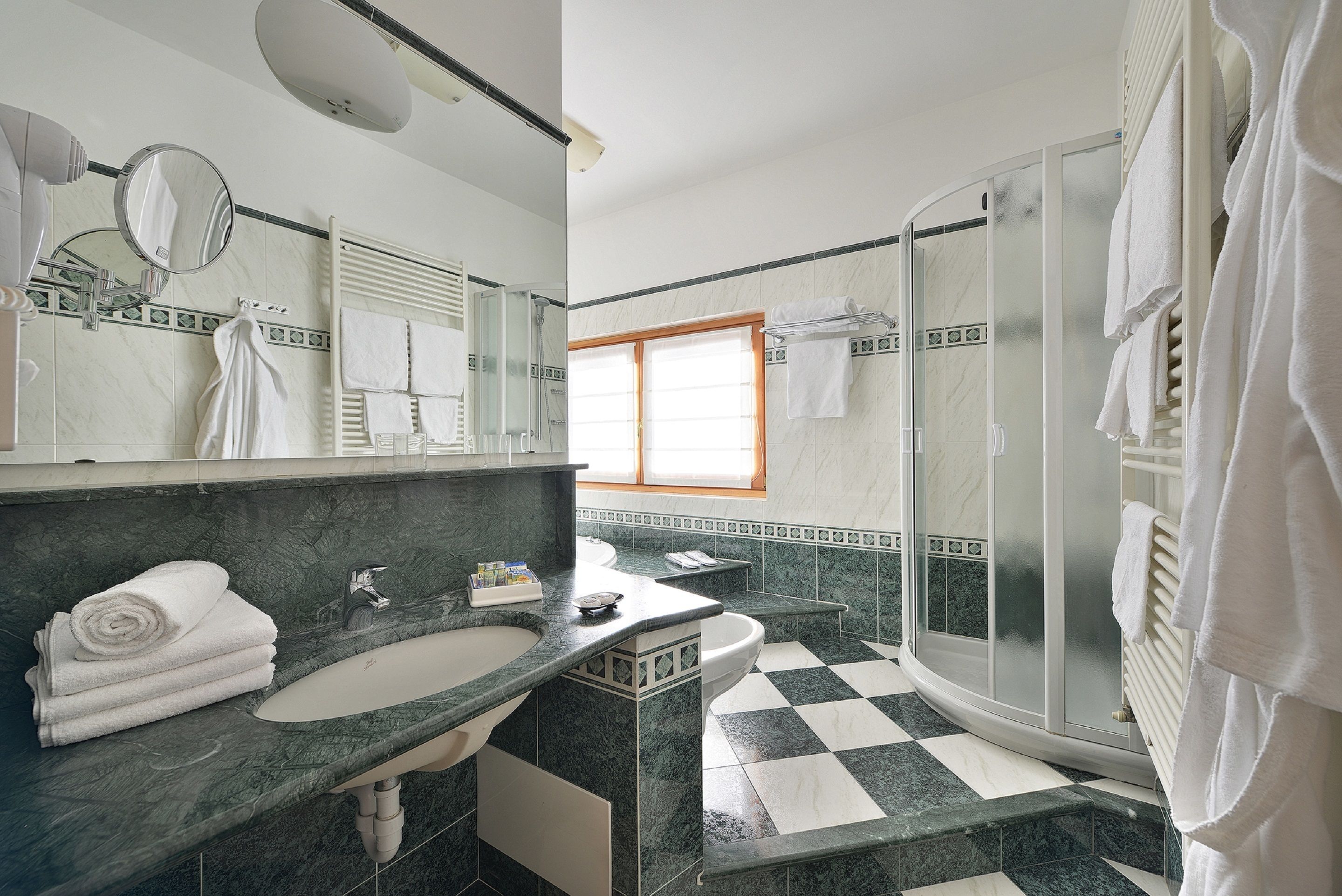 Un baño con piso a cuadros, dos lavamanos, cabina de ducha de vidrio y un espejo grande.
