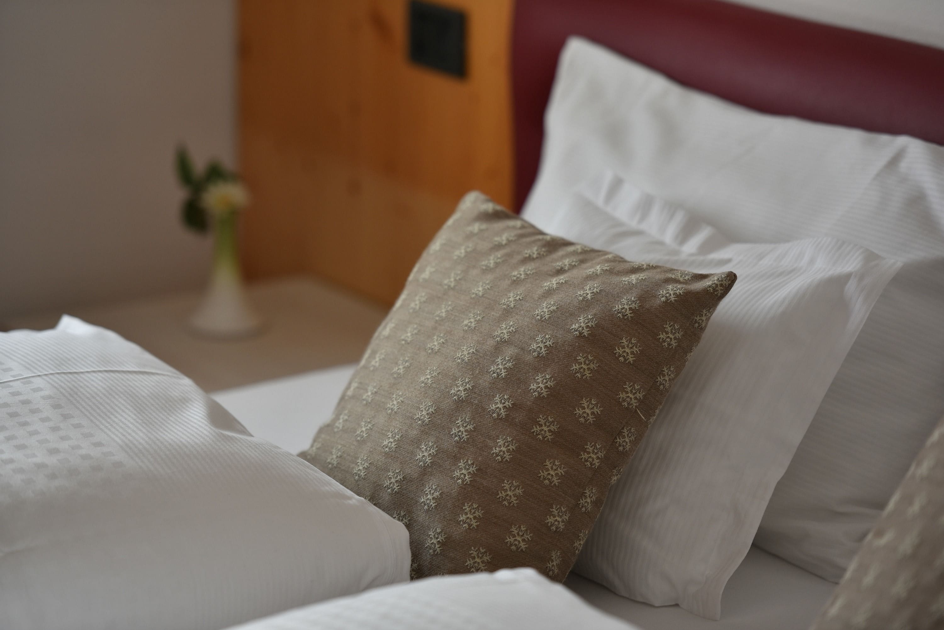 A neatly made bed with white and patterned pillows, a small vase with a plant, and a wooden headboard.