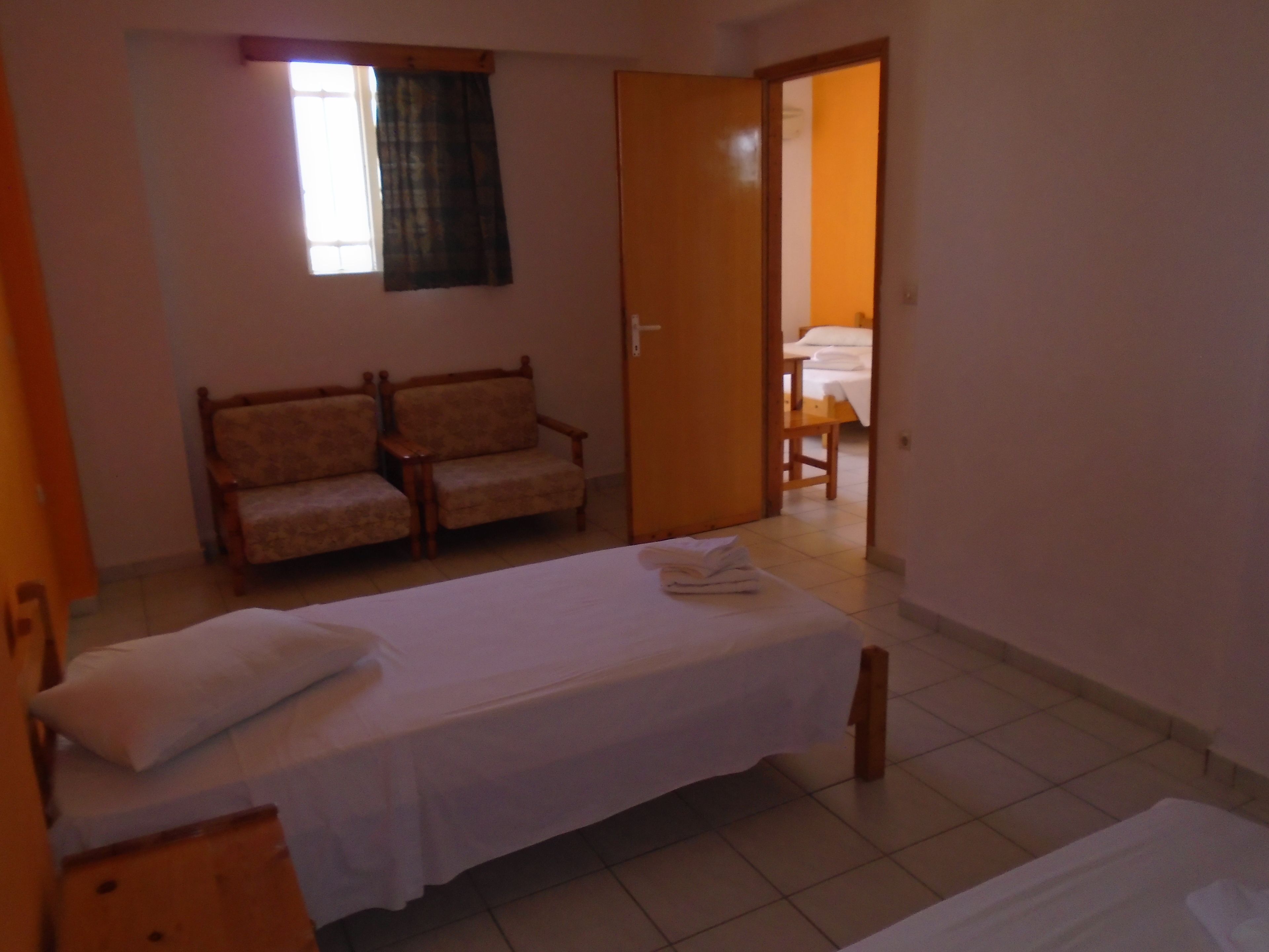 Quarto com duas camas de solteiro, um banco de madeira, um sofá e uma pequena mesa.