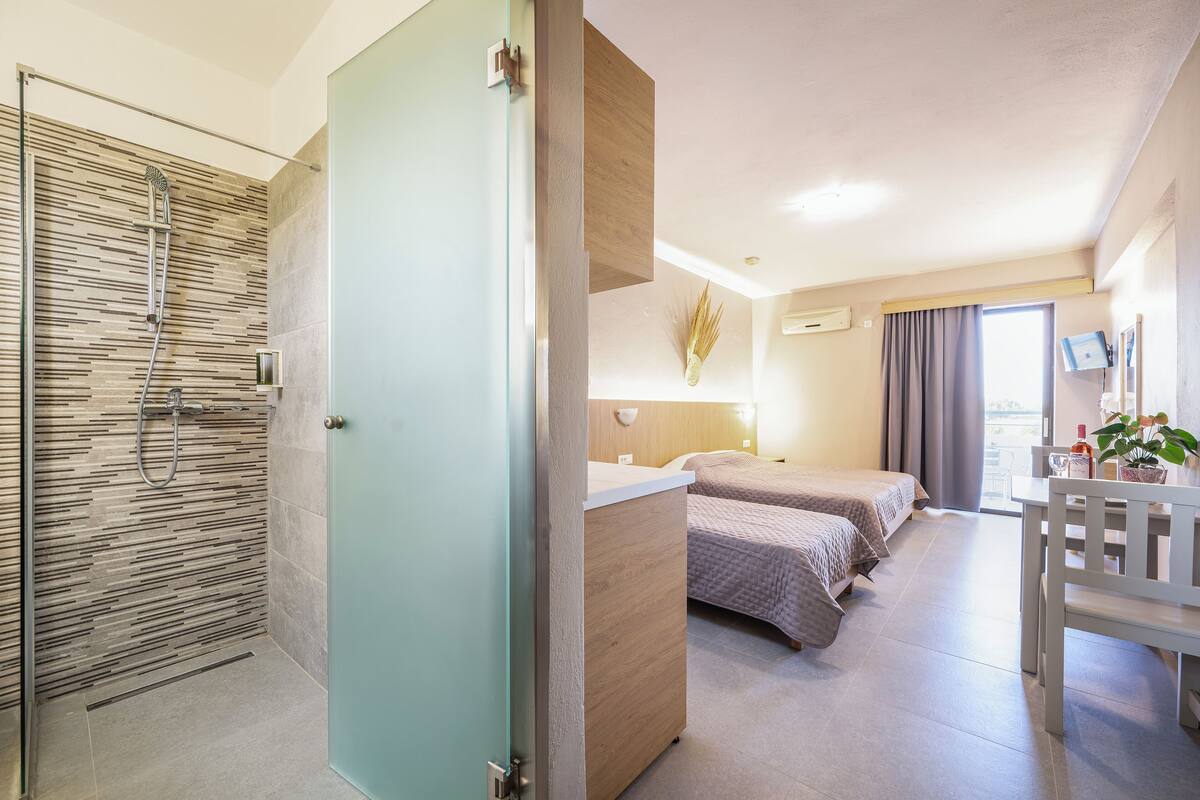 A modern hotel room with a shower, two beds, a desk, and a view of the outdoors.