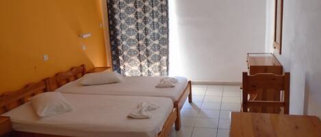 A room with two wooden beds, a wooden desk, and a window with patterned curtains.