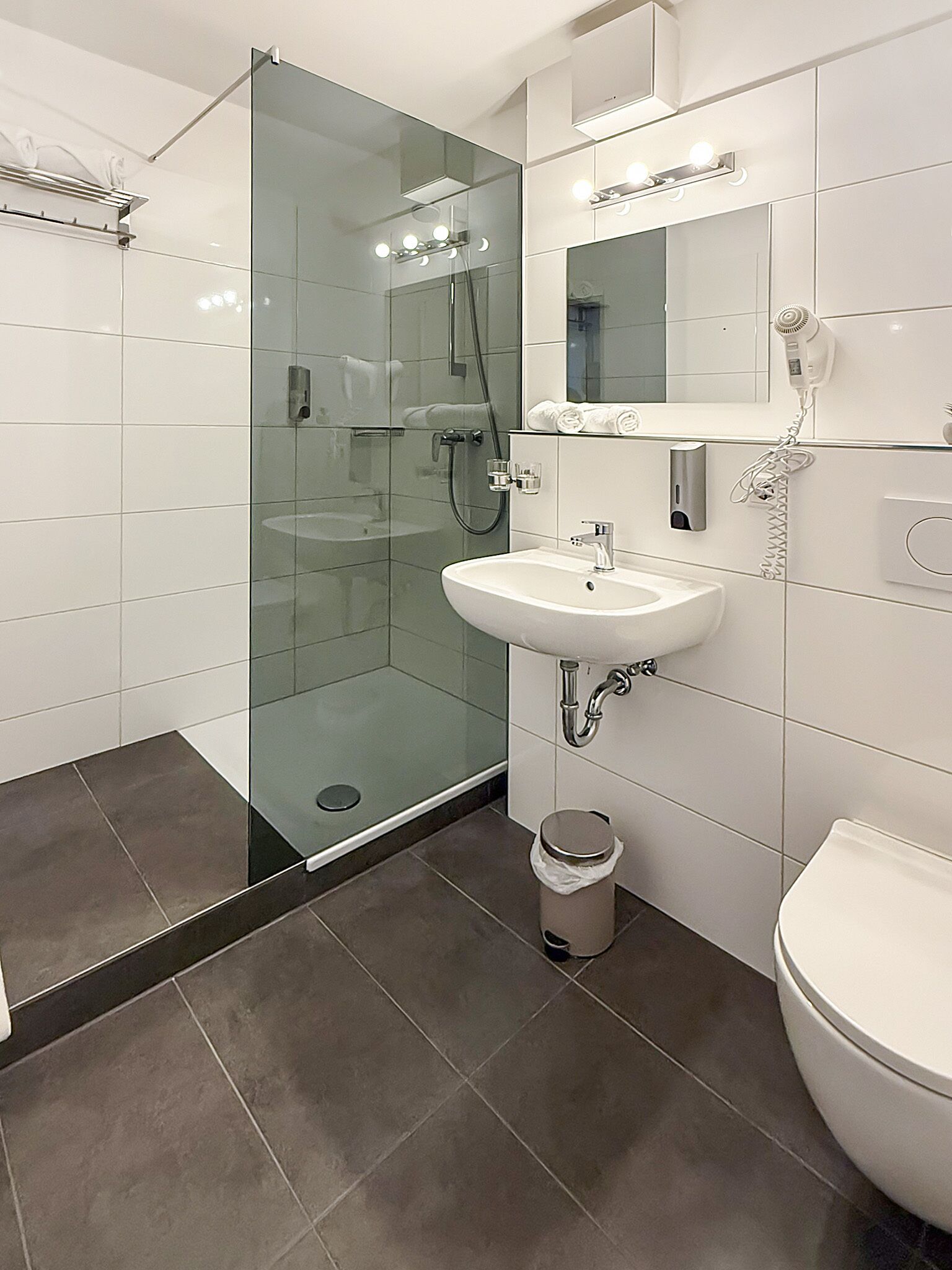 A modern bathroom with a glass-enclosed shower, a white sink, and a toilet.