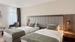 A hotel room with two beds, a desk, a chair, and a window with curtains. - STADT-Hotel Lörrach (Loerrach)