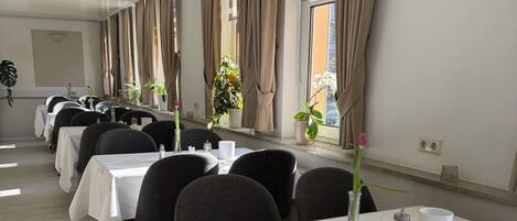 Un salón de conferencias con varias mesas, sillas y plantas en macetas.