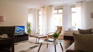 A modern living room with a sofa, a glass coffee table, a TV, and a chair. - STADT-Hotel Lörrach (Loerrach)