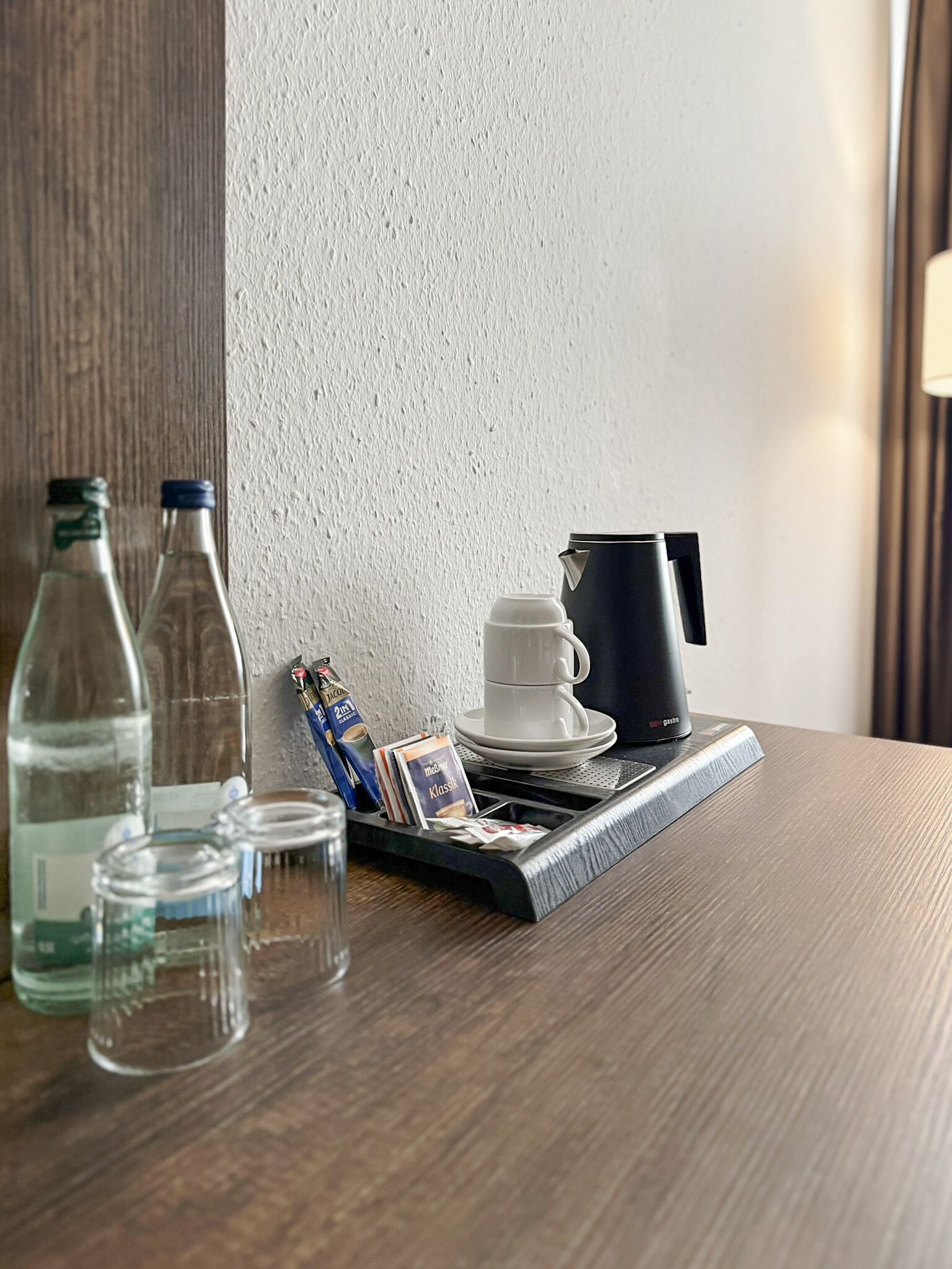 Ein ordentlich gedeckter Tisch mit einer Kaffeemaschine, einer Tasse, einer Tablett mit Kaffeekapseln und Wasserflaschen.