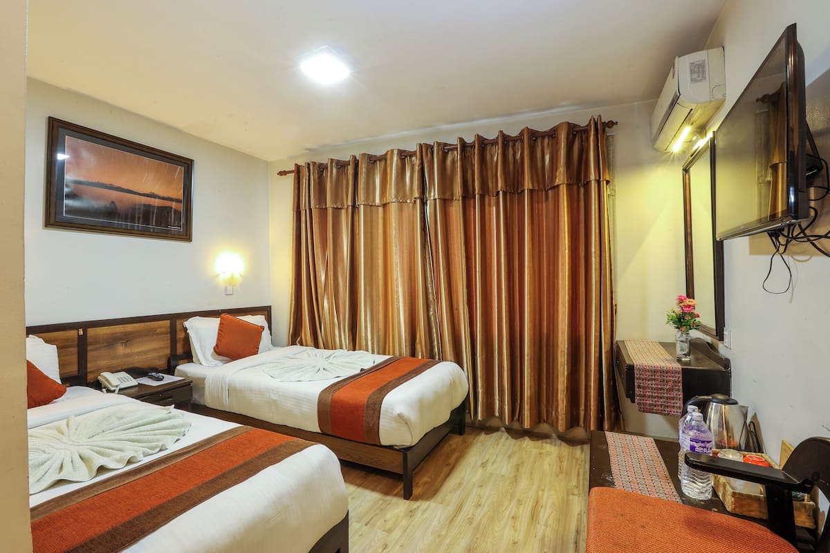 A hotel room with two beds, a flat-screen TV, a mirror, and a small table with a water bottle and a box.