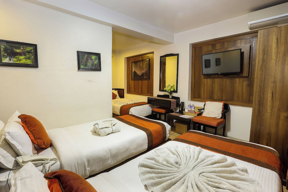 A hotel room with two beds, a desk, a chair, a television, and artwork on the walls.