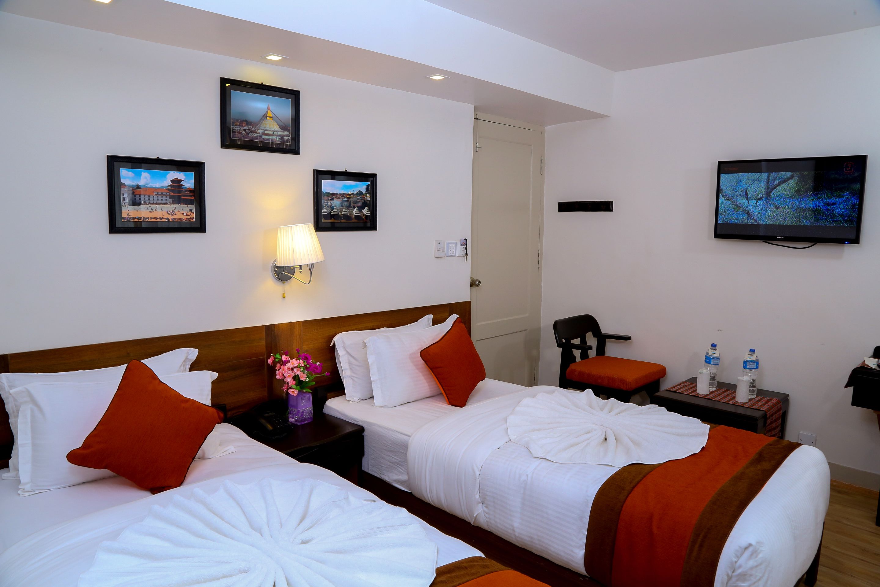 A hotel room with two beds, a TV, and a nightstand with a lamp and water bottles.