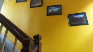 A staircase with a wooden handrail and a yellow wall with five framed pictures. - Hotel Outfitter Nepal (Kathmandu)