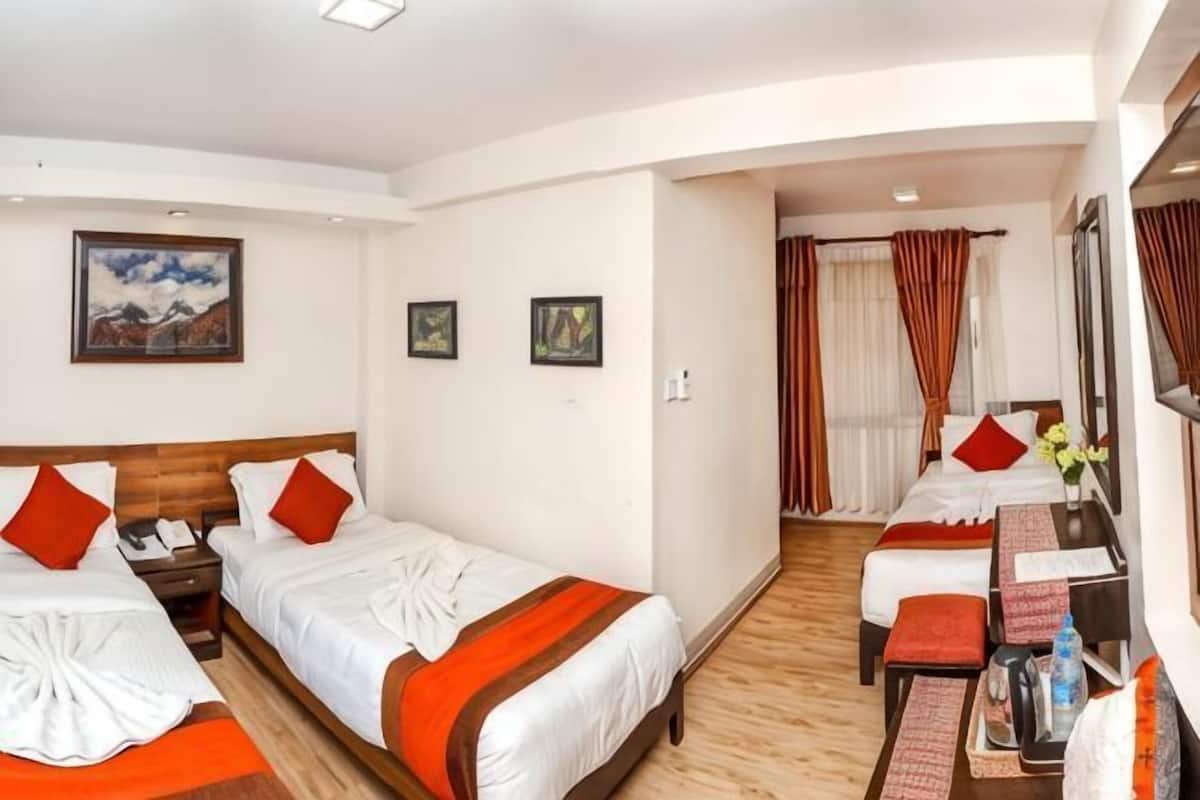 A hotel room with two beds, a desk, and a chair. There are pictures on the wall, a window with curtains, and a wooden floor.