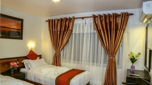 A hotel room with two beds, a desk, a chair, and a window with curtains. - Hotel Outfitter Nepal (Kathmandu)