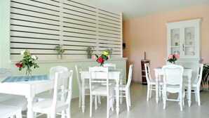 Un comedor con mobiliario blanco, mantel a rayas y plantas en macetas sobre una pared verde claro.