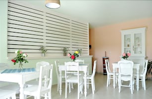 Un comedor con mobiliario blanco, mantel a rayas y plantas en macetas sobre una pared verde claro.