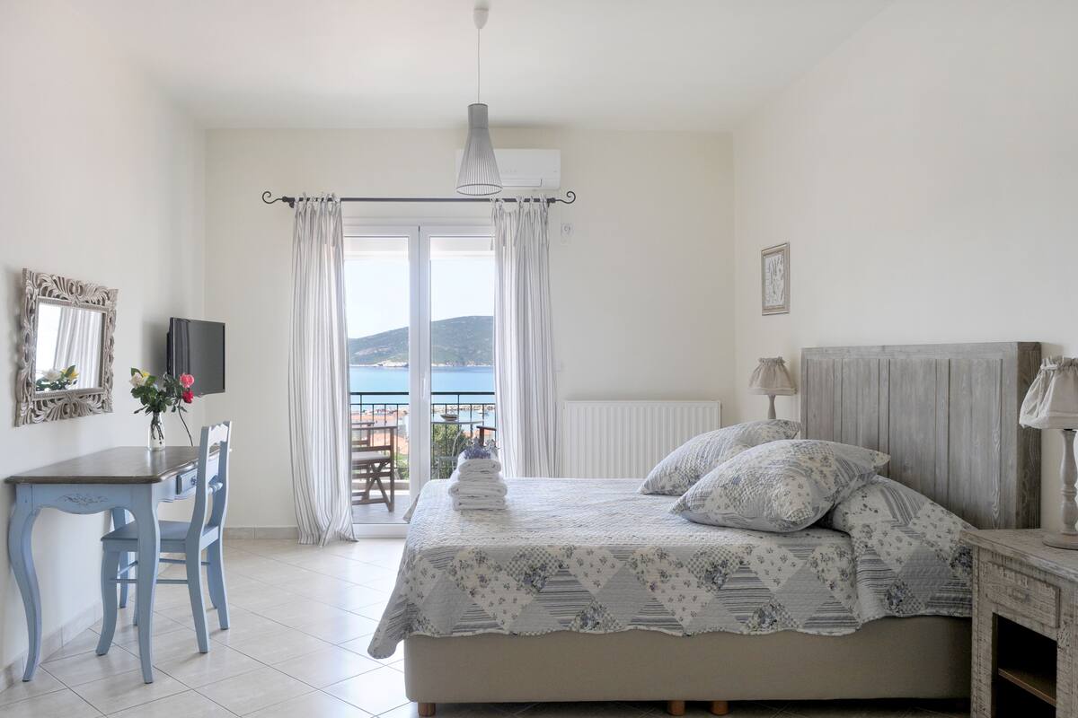 Une chambre avec un lit, un bureau, une chaise, une télévision et une vue sur la mer.