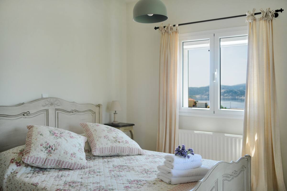 Une chambre à coucher avec un lit, une table de chevet, une lampe et une fenêtre avec des rideaux.