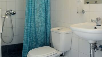 Um banheiro com vaso sanitário, pia, chuveiro com cortina azul estampada e espelho.